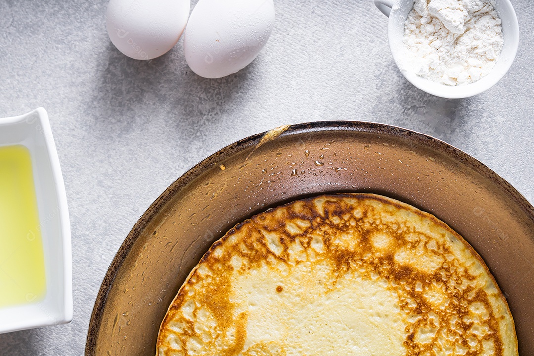 Deliciosas panquecas em uma frigideira sobre uma mesa branca, com trigo, ovos, azeite, molho de tomate e uma toalha xadrez ao fundo