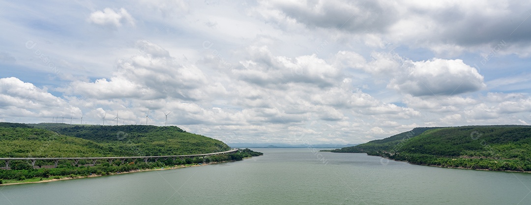 Paisagem de montanha verde com parque eólico e reservatório de água com céu azul e nuvens brancas