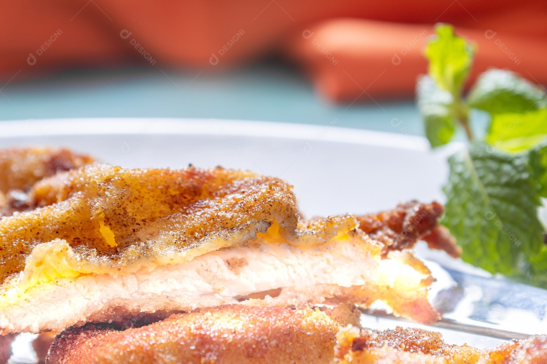 Delicioso frango à milanesa (frango empanado com farinha de rosca e ovo), prato típico brasileiro. Em um prato branco com tomate, limão no mármore azul. Detalhe do bife cortado ao meio.