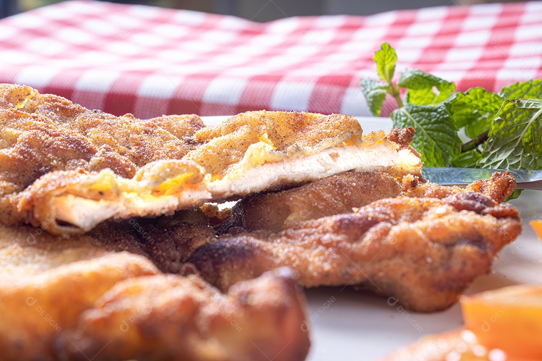 Delicioso frango à milanesa (frango empanado com farinha de rosca e ovo), prato típico brasileiro. Em um prato branco com tomate, limão no mármore azul. Detalhe do bife cortado ao meio.