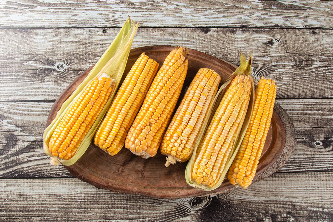 Milho amarelo fresco em madeira rústica e fundo desfocado verde.