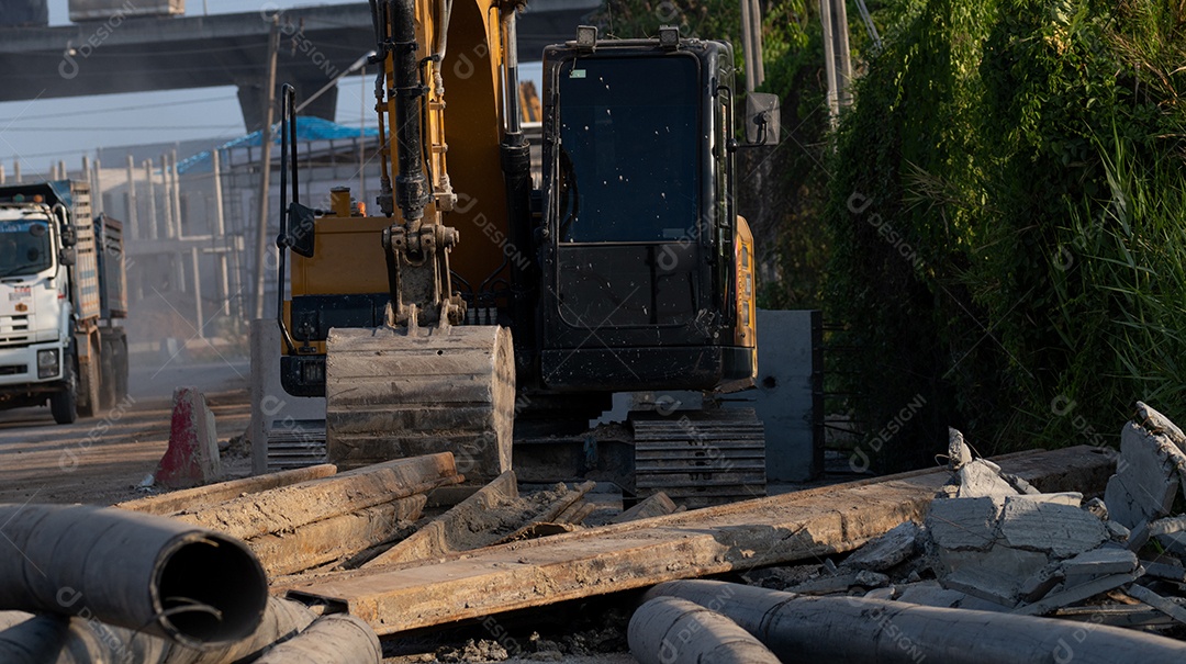 Escavadeira de madeira estacionada no canteiro de obras com caminhão desfocado dirigindo na estrada e projeto de construção de condomínio