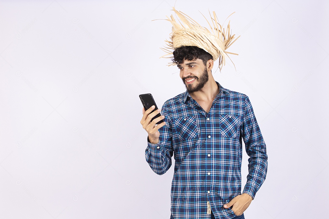 Homem jovem barbudo fantasiada celebrando festas juninas segurando celular smartphone