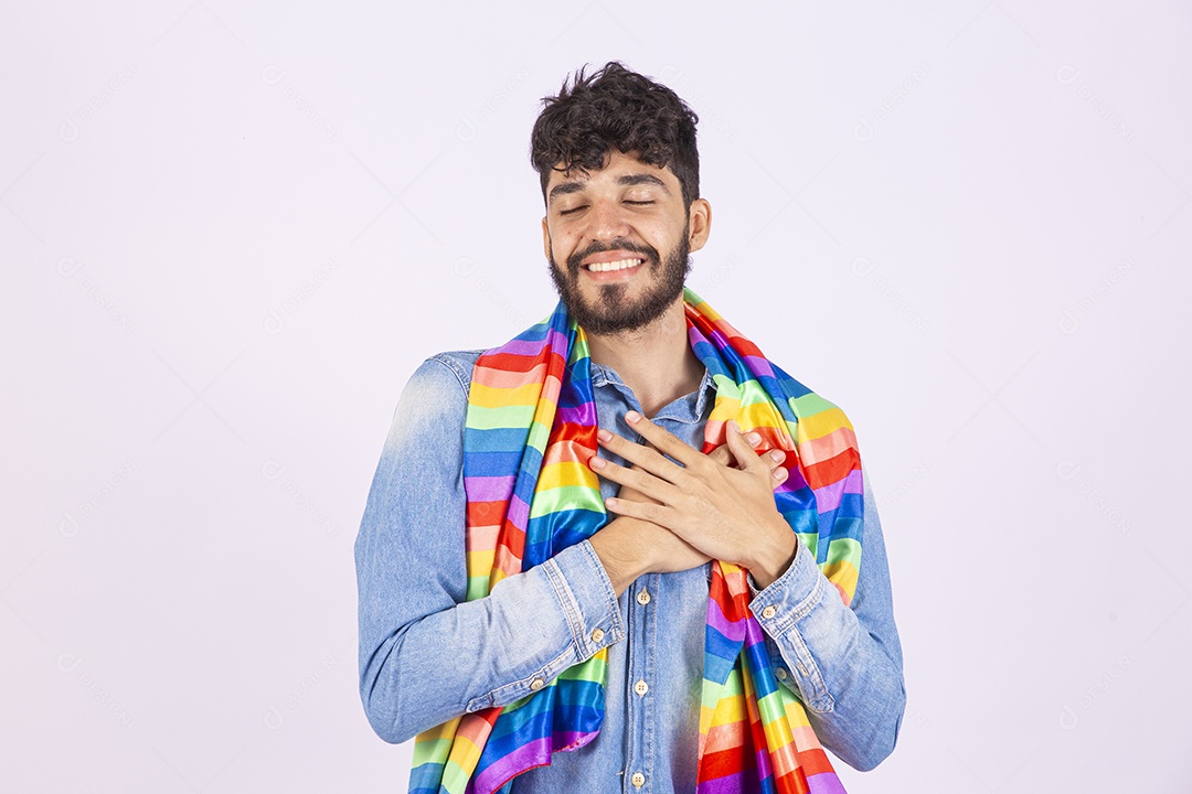 Homem jovem feliz e sorridente sobre fundo isolado branco segurando bandeira LGBTQI+