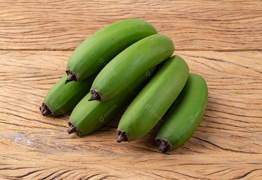 Um cacho de bananas verdes sobre a mesa de madeira.