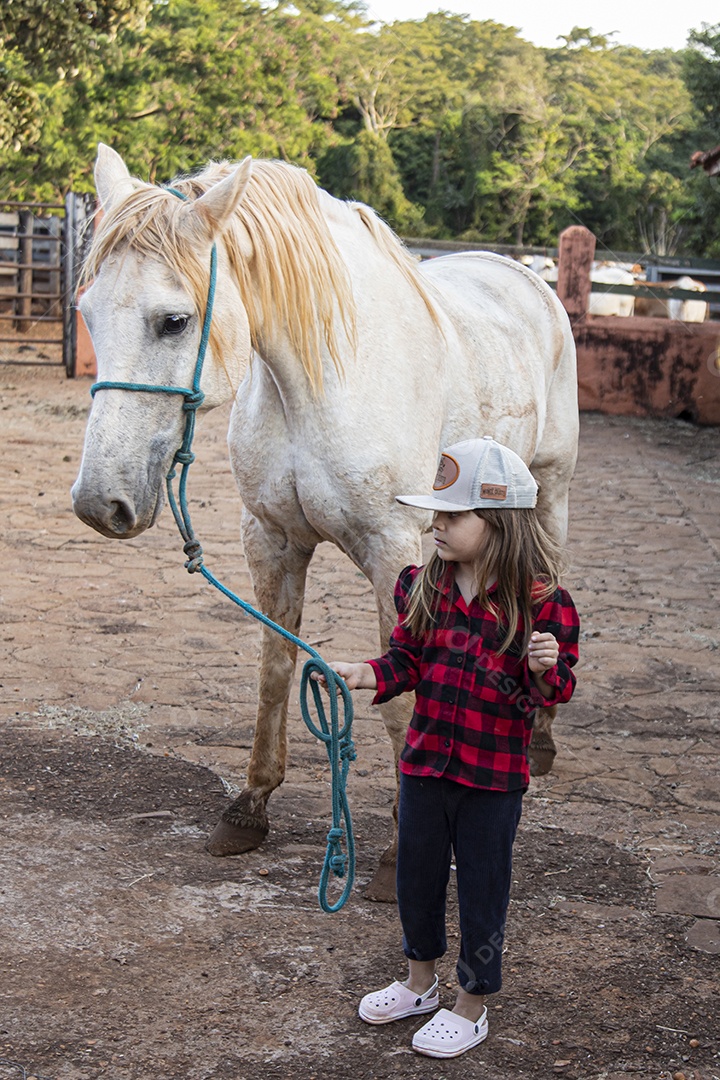 Menina feliz e sorridente sobre fazenda ao lado de seu cavalo