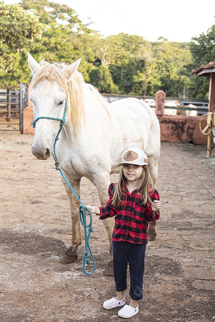 Menina feliz e sorridente sobre fazenda ao lado de seu cavalo