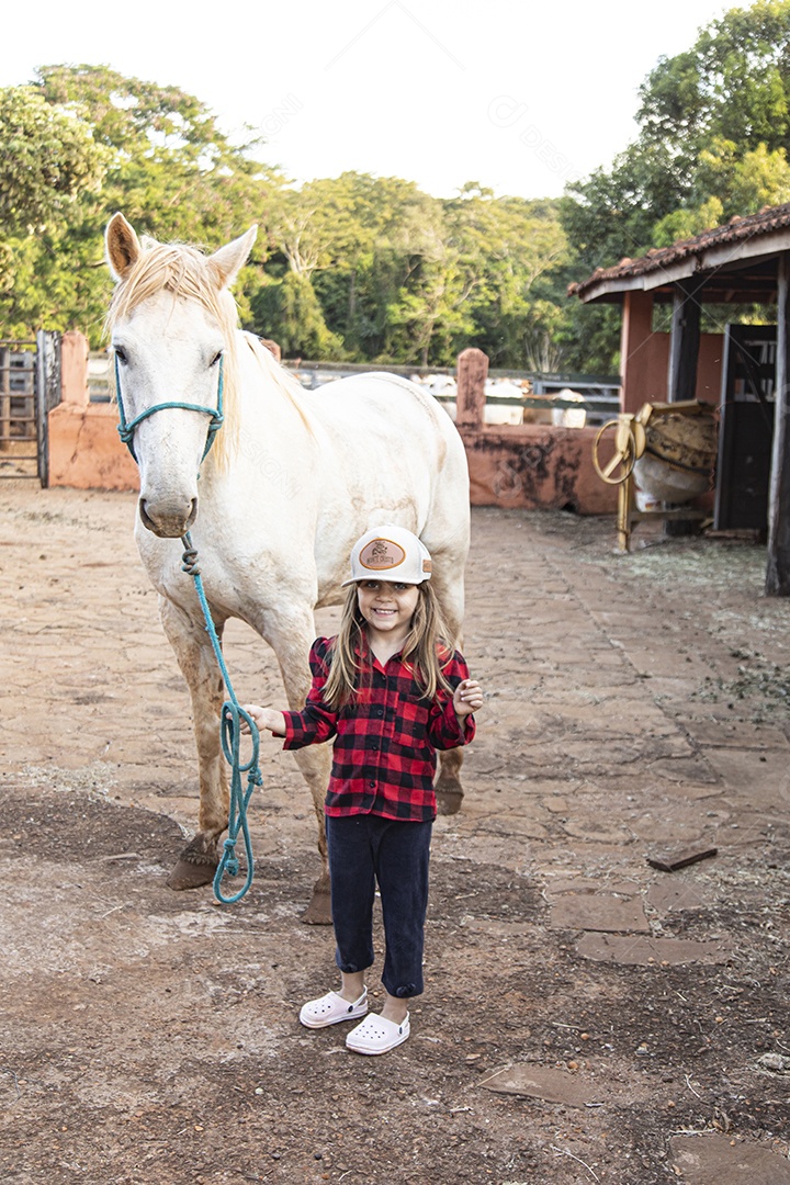 Menina feliz e sorridente sobre fazenda ao lado de seu cavalo