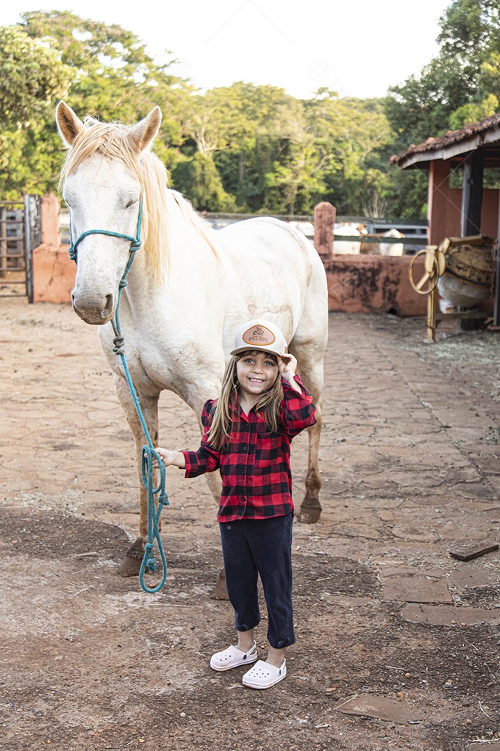 Menina feliz e sorridente sobre fazenda ao lado de seu cavalo
