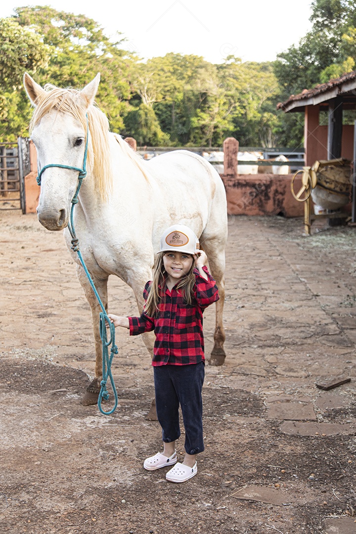 Menina feliz e sorridente sobre fazenda ao lado de seu cavalo
