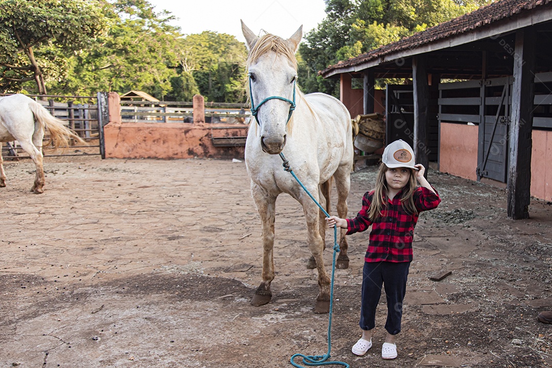 Menina feliz e sorridente sobre fazenda ao lado de seu cavalo