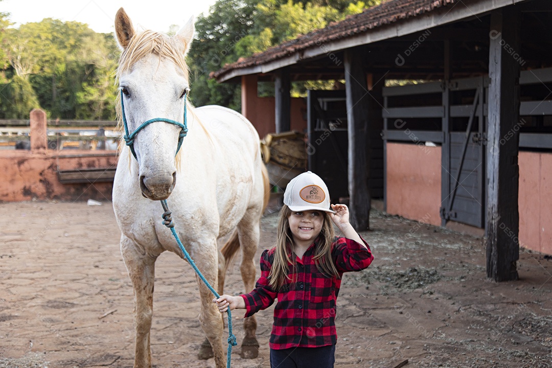 Menina feliz e sorridente sobre fazenda ao lado de seu cavalo
