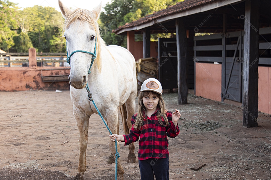 Menina feliz e sorridente sobre fazenda ao lado de seu cavalo