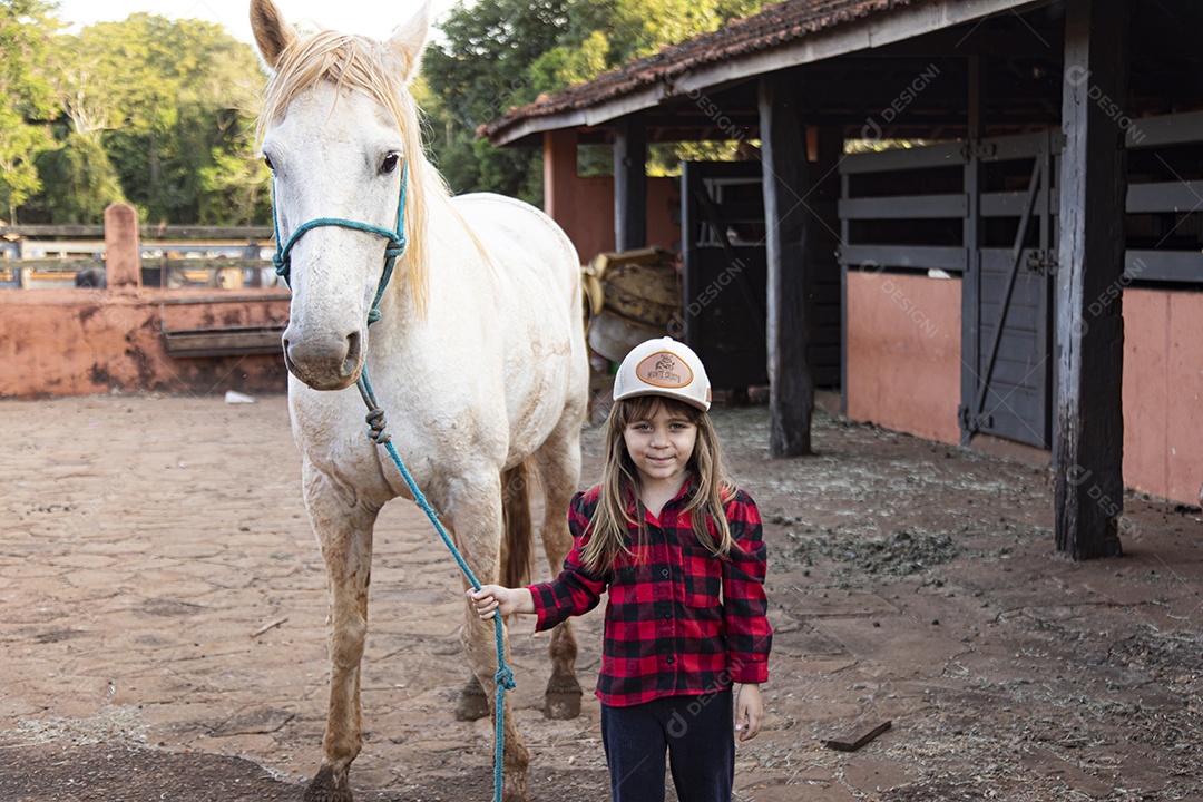 Menina feliz e sorridente sobre fazenda ao lado de seu cavalo