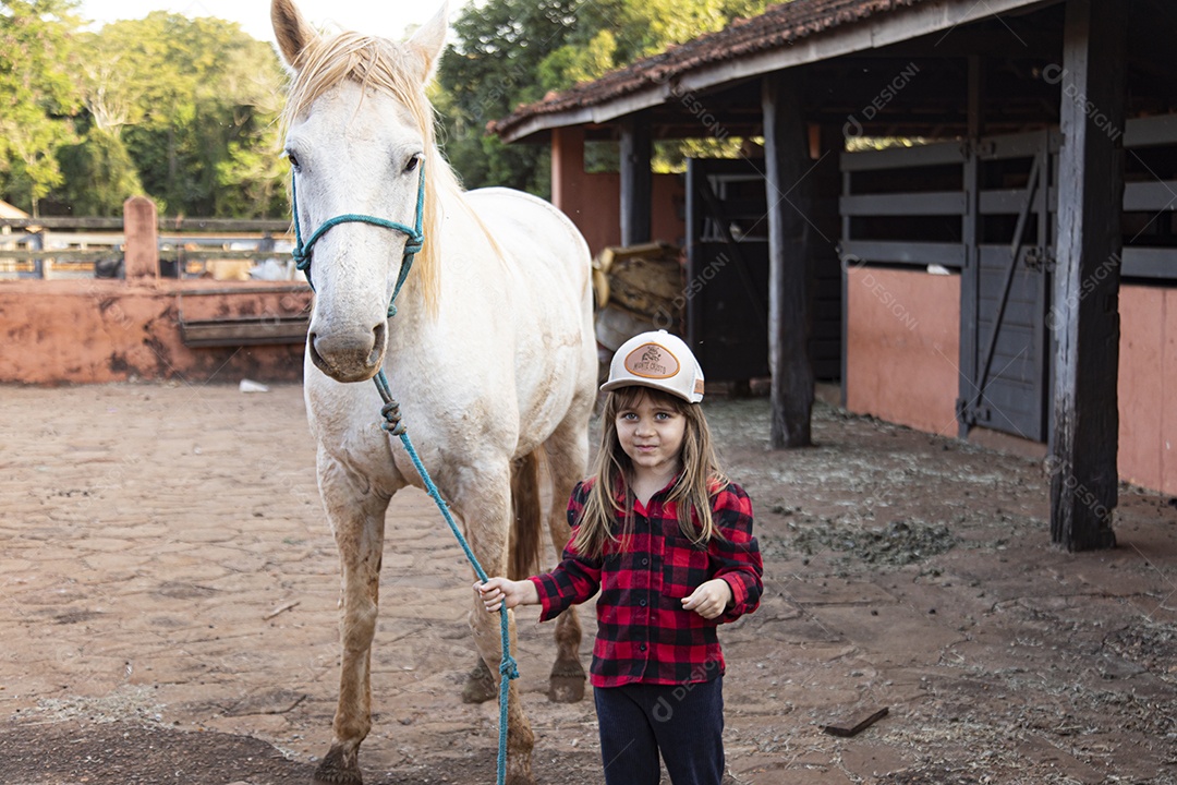 Menina feliz e sorridente sobre fazenda ao lado de seu cavalo
