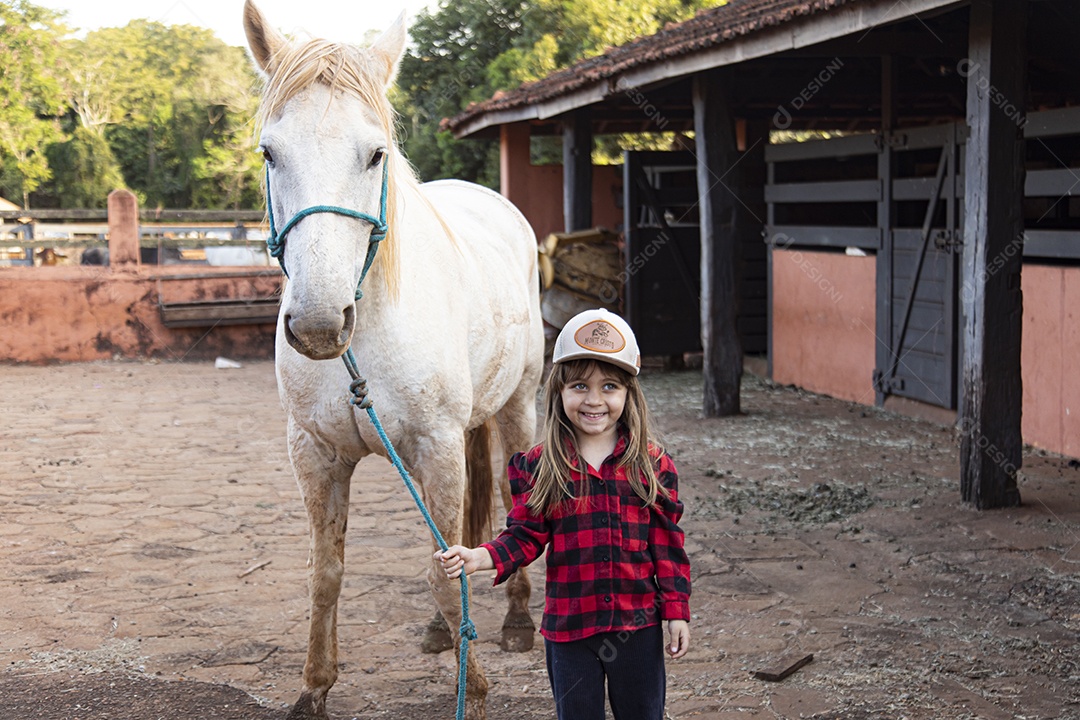 Menina feliz e sorridente sobre fazenda ao lado de seu cavalo
