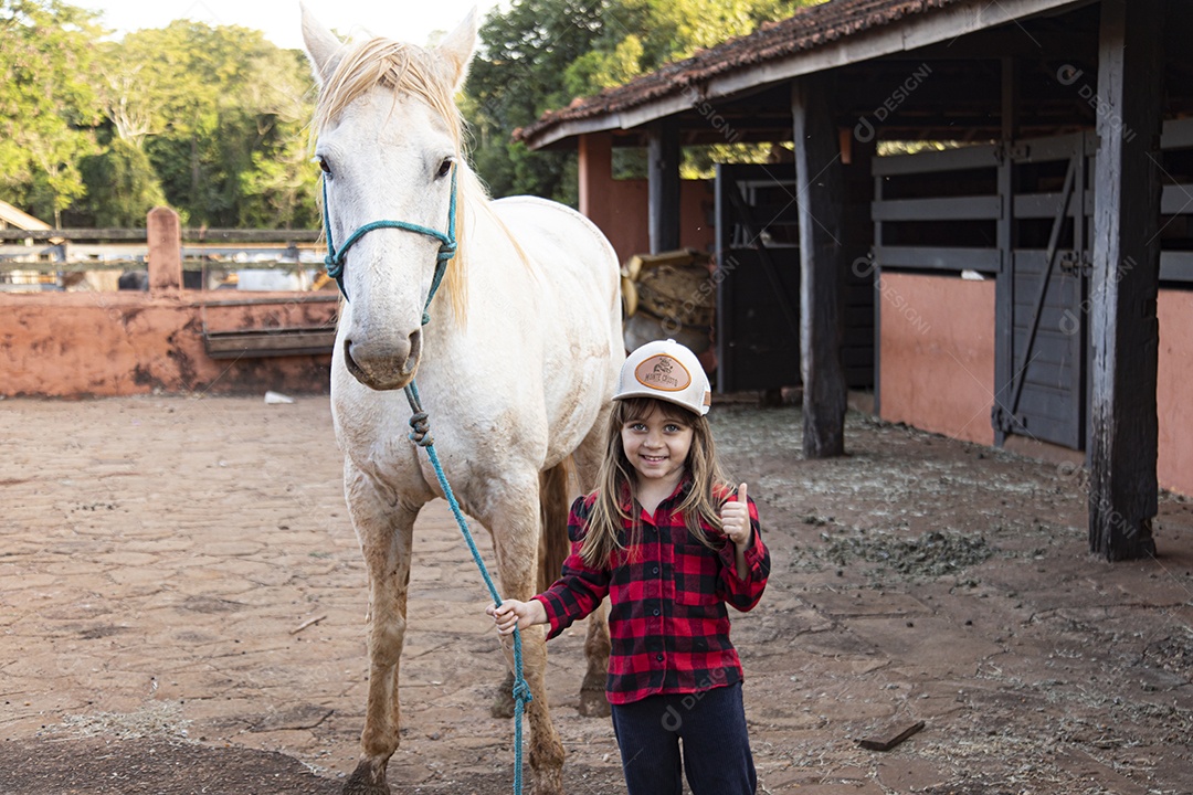 Menina feliz e sorridente sobre fazenda ao lado de seu cavalo