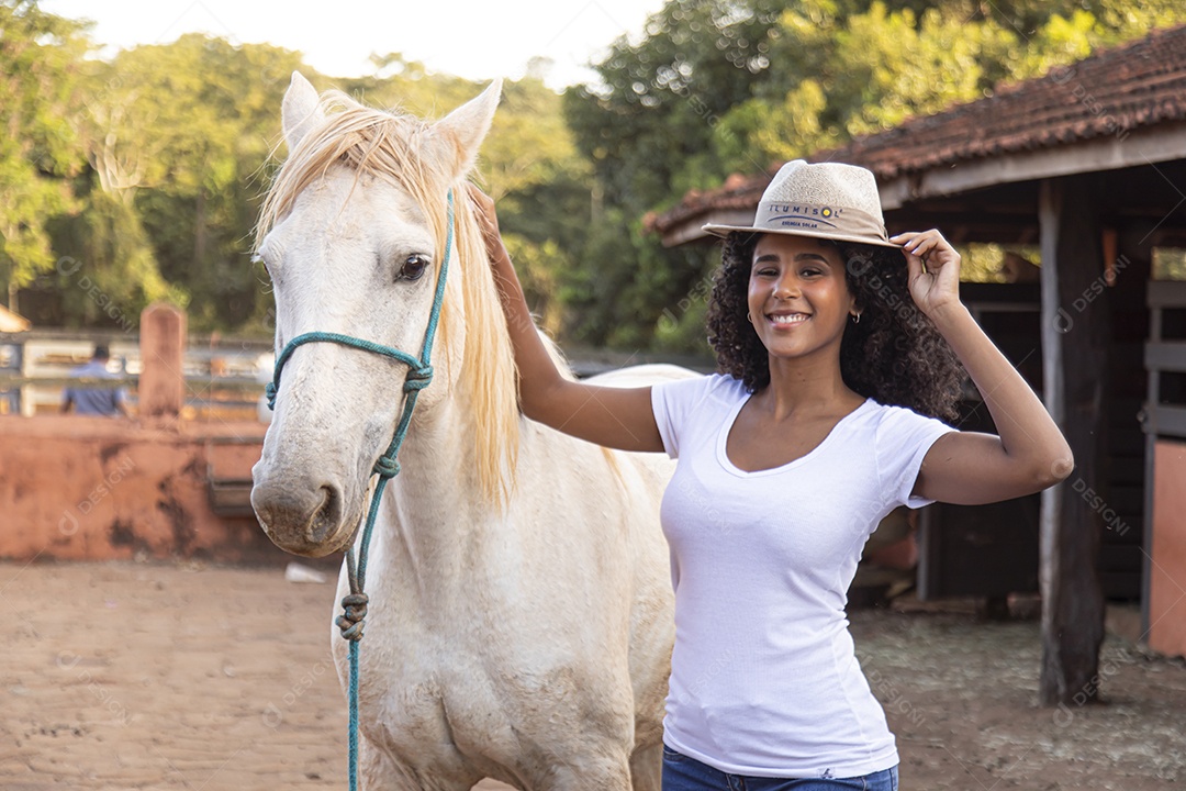 Mulher jovem cabelo cacheado ao lado de seu cavalo em uma fazenda