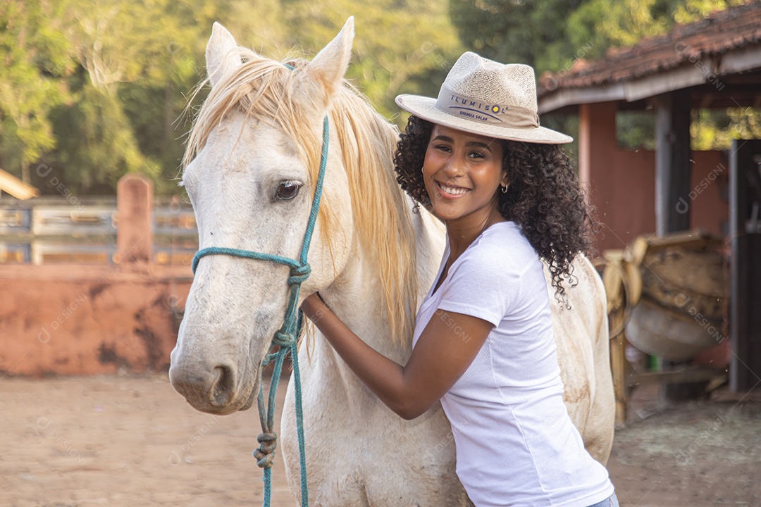 Mulher jovem feliz e sorridente sobre fazenda ao lado de seu cavalo