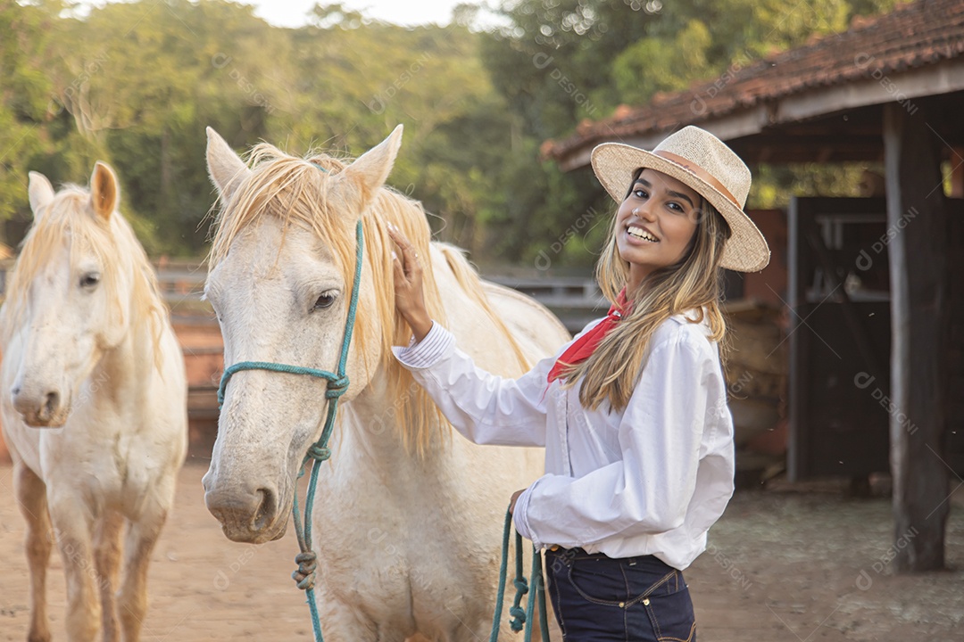 Mulher jovem feliz e sorridente sobre fazenda ao lado de seu cavalo
