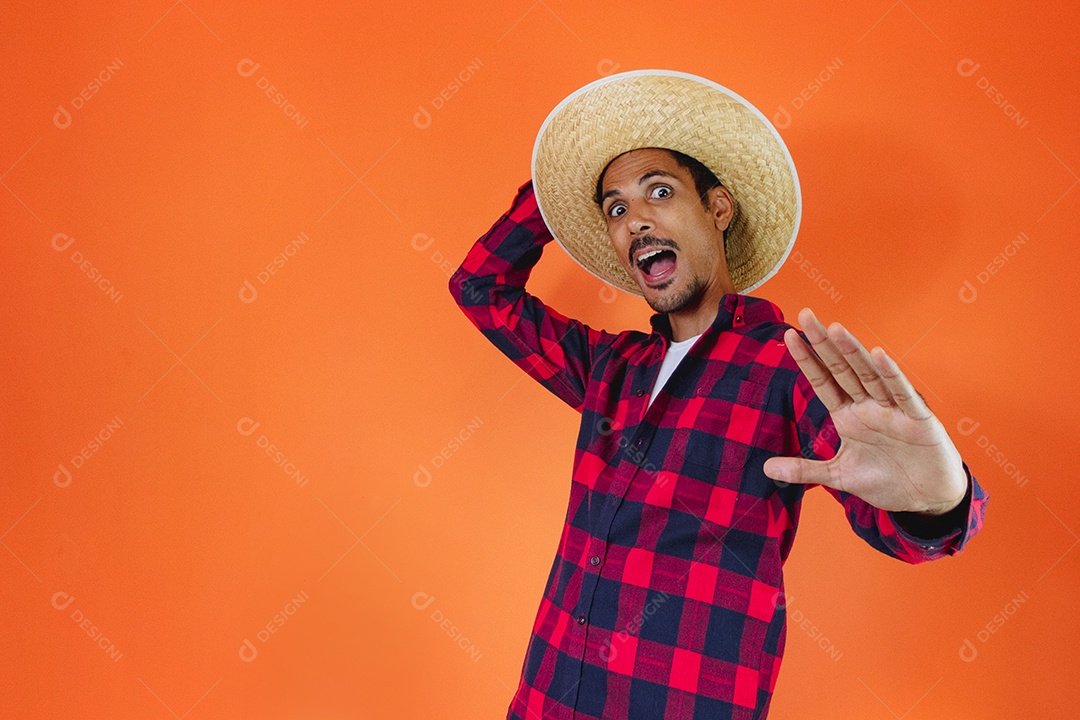 Festa Junina. Homem negro com roupa segurando um celular isolado em fundo laranja.