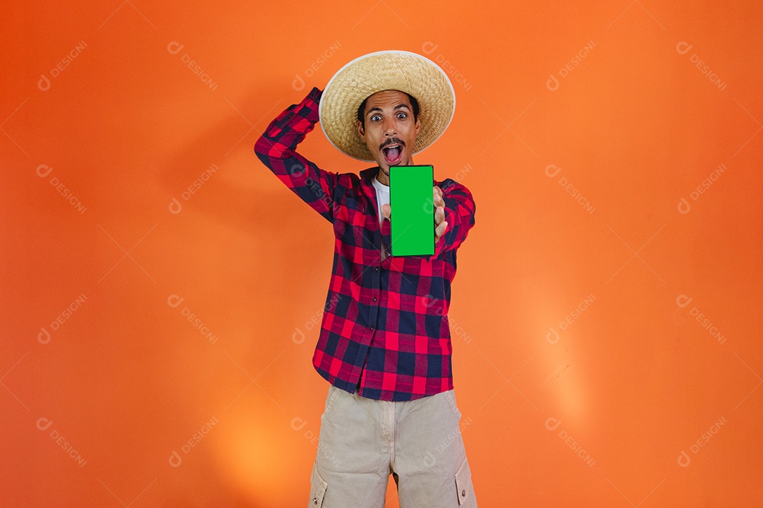 Festa Junina. Homem negro com roupa segurando um celular isolado em fundo laranja.