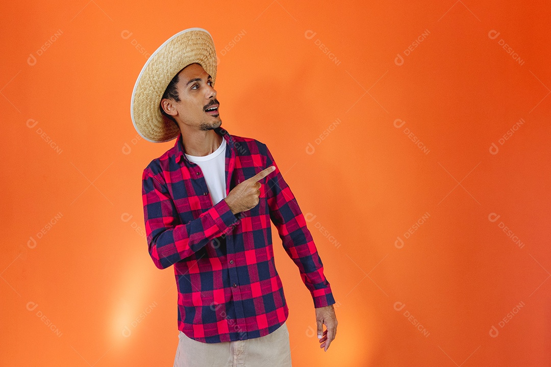 Festa Junina. Homem negro com roupa segurando um celular isolado em fundo laranja.