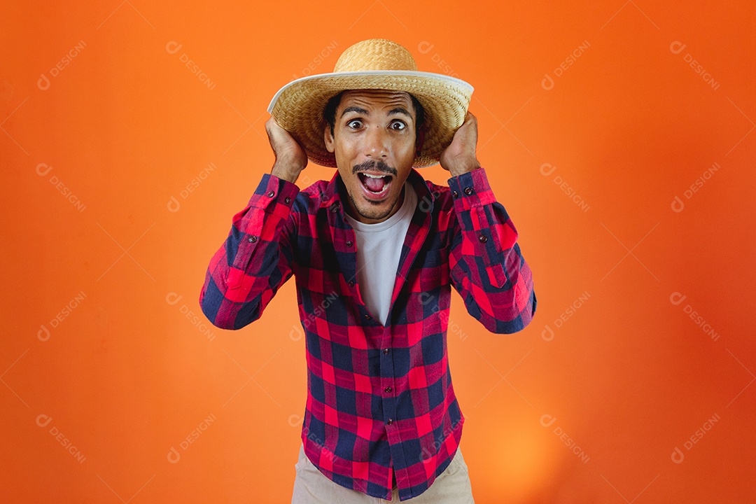 Festa Junina. Homem negro com roupa segurando um celular isolado em fundo laranja.