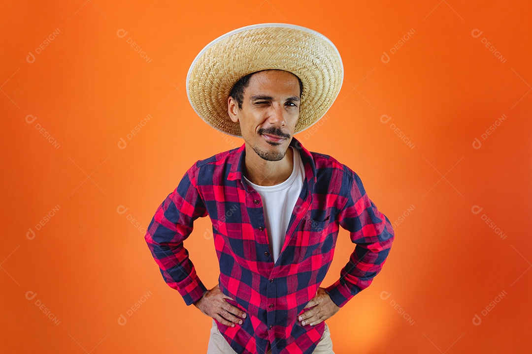 Festa Junina. Homem negro com roupa segurando um celular isolado em fundo laranja.