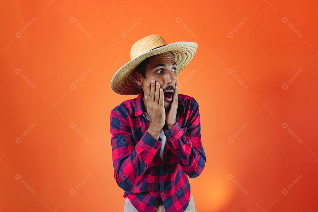 Festa Junina. Homem negro com roupa segurando um celular isolado em fundo laranja.
