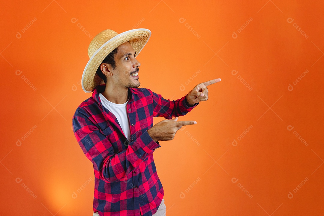 Festa Junina. Homem negro com roupa segurando um celular isolado em fundo laranja.