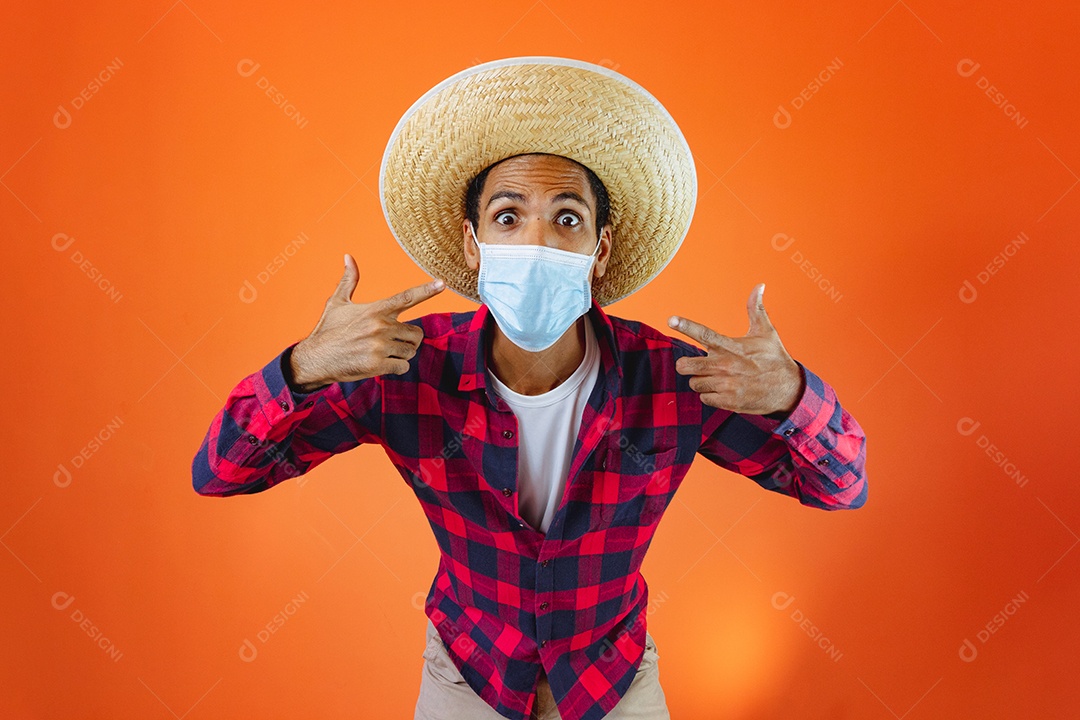 Festa Junina. Homem negro com roupa segurando um celular isolado em fundo laranja.