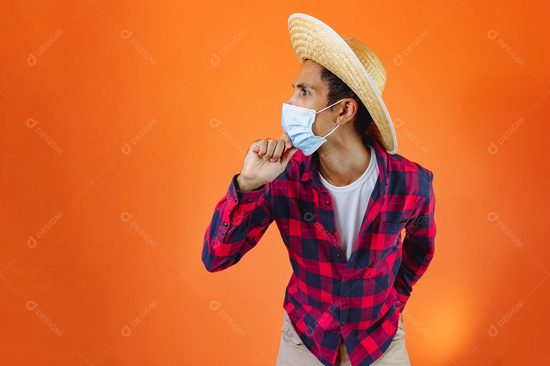 Festa Junina. Homem negro com roupa segurando um celular isolado em fundo laranja.
