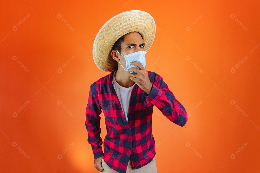 Festa Junina. Homem negro com roupa segurando um celular isolado em fundo laranja.