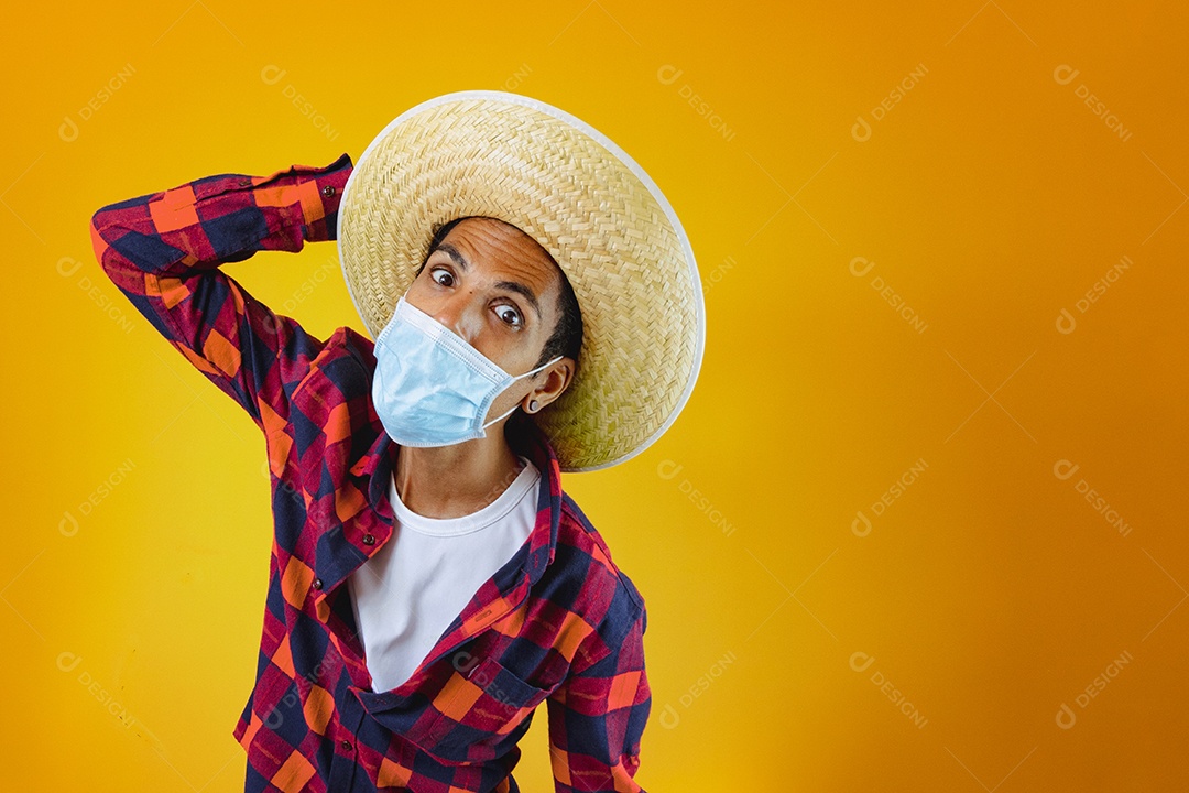 Homem negro com roupa de festa junina com máscara pandêmica isolada em fundo amarelo.