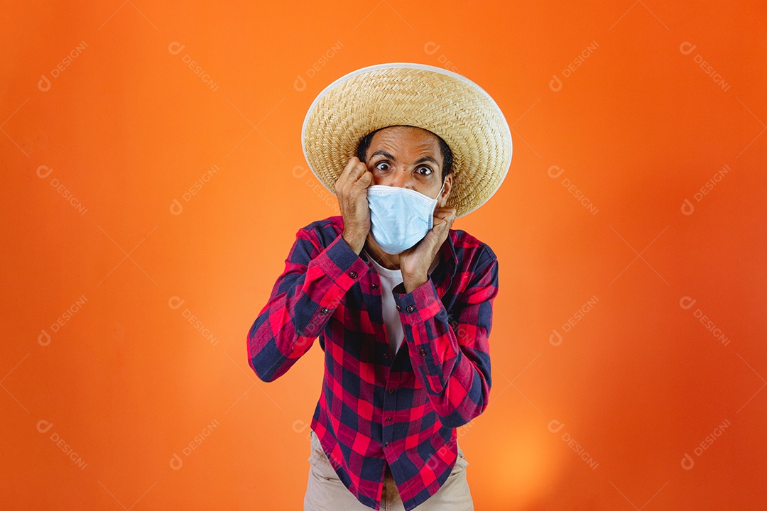Homem negro com roupa de festa junina com máscara pandêmica isolada em fundo laranja.