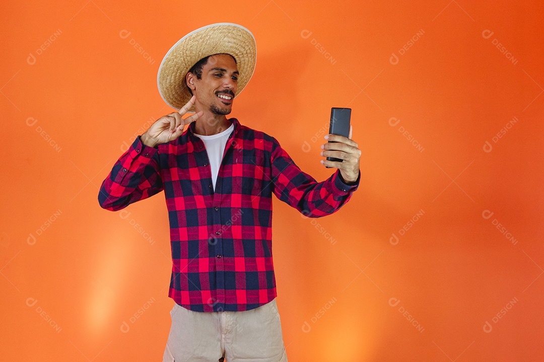 Festa Junina. Homem negro com roupa apontando isolado em fundo laranja.