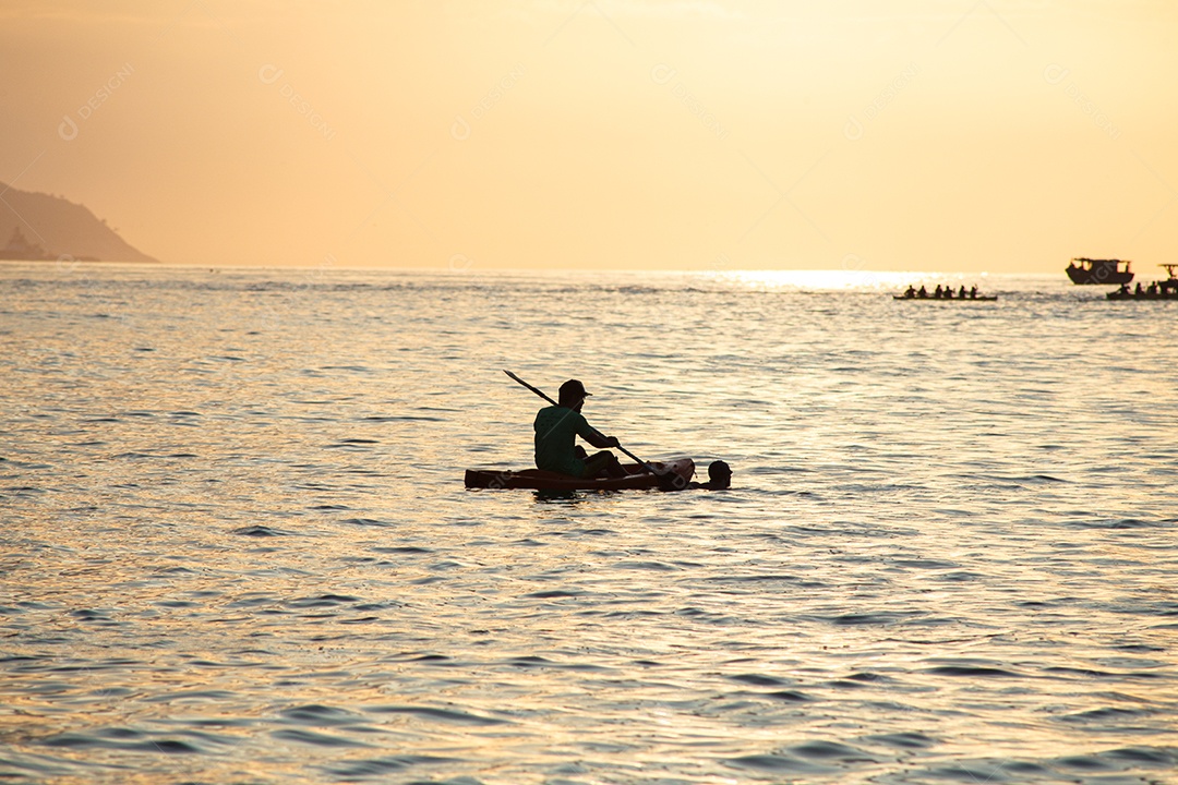 silhuetas de pessoas em canoas ao amanhecer na praia de Copacabana, no Rio de Janeiro