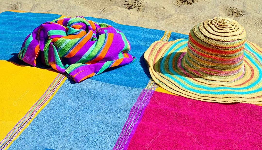 Chapéu colorido e toalha na areia da praia