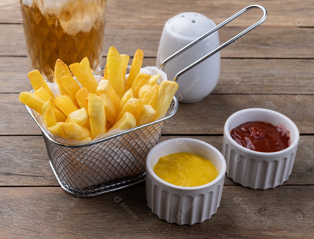 Batatas fritas em uma cesta com sal, ketchup, mostarda e um copo de refrigerante sobre a mesa de madeira