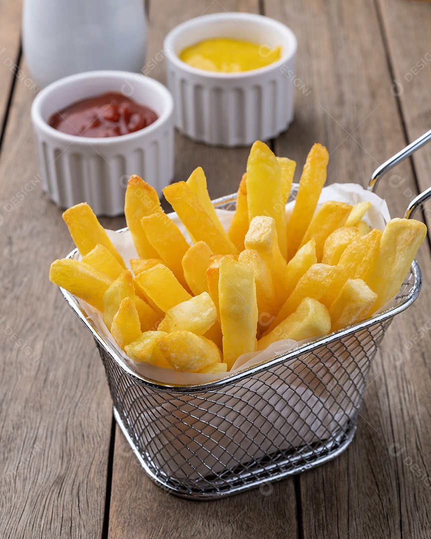 Batatas fritas em uma cesta com sal, ketchup, mostarda e um copo de refrigerante sobre a mesa de madeira