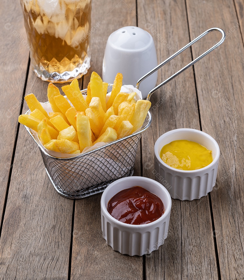 Batatas fritas em uma cesta com sal, ketchup, mostarda e um copo de refrigerante sobre a mesa de madeira.