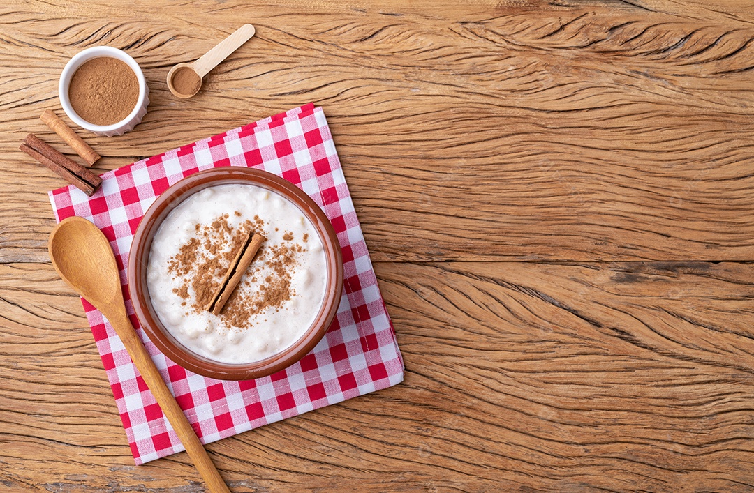 Canjica ou munguza, típico creme doce de milho branco brasileiro com canela sobre mesa de madeira com espaço para cópia.