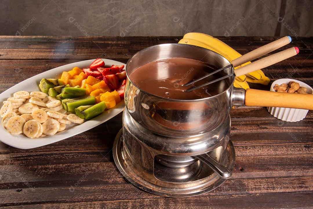 Fondue de chocolate acompanhado de frutas tropicais na mesa de madeira e fundo escuro