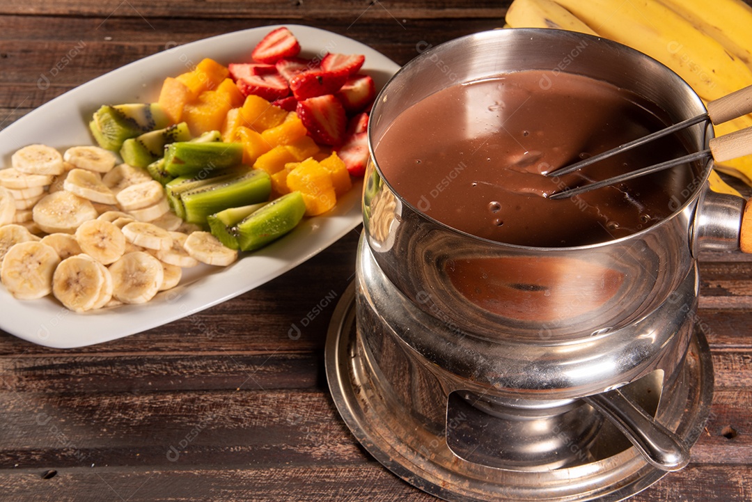 Fondue de chocolate acompanhado de frutas tropicais na mesa de madeira e fundo escuro