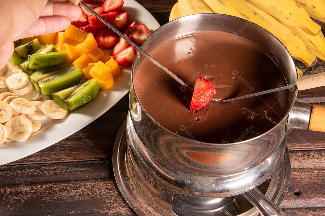 Fondue de chocolate acompanhado de frutas tropicais na mesa de madeira e fundo escuro