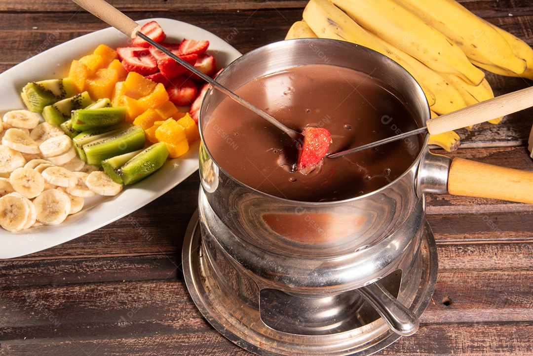 Fondue de chocolate acompanhado de frutas tropicais na mesa de madeira e fundo escuro
