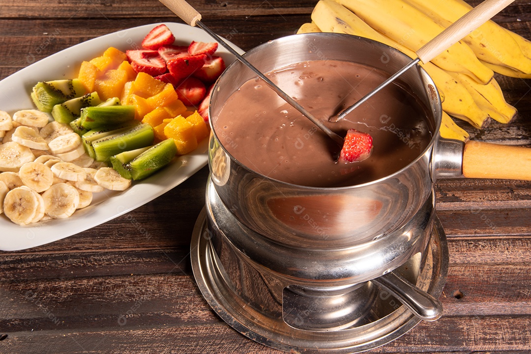 Fondue de chocolate acompanhado de frutas tropicais na mesa de madeira e fundo escuro