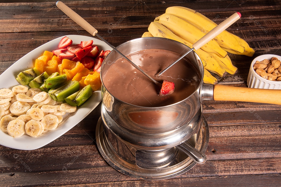 Fondue de chocolate acompanhado de frutas tropicais na mesa de madeira e fundo escuro
