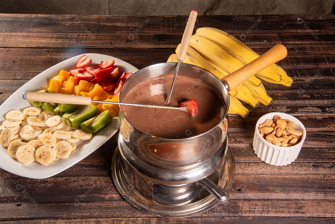 Fondue de chocolate acompanhado de frutas tropicais na mesa de madeira e fundo escuro